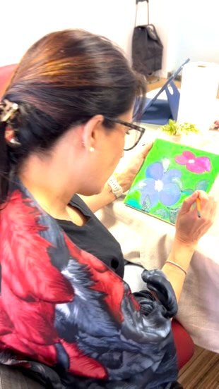 mujer pintando una flor azul sobre fondo verde en un encuentro creativo de Hechizarte